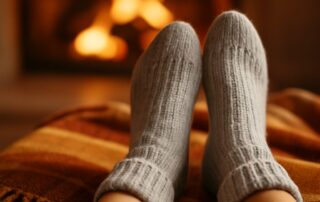 Cozy feet in thick gray socks resting on a warm plaid blanket near a fireplace, illustrating cold feet and fall foot care for Canton Foot and Ankle Specialists, Canton Podiatry.