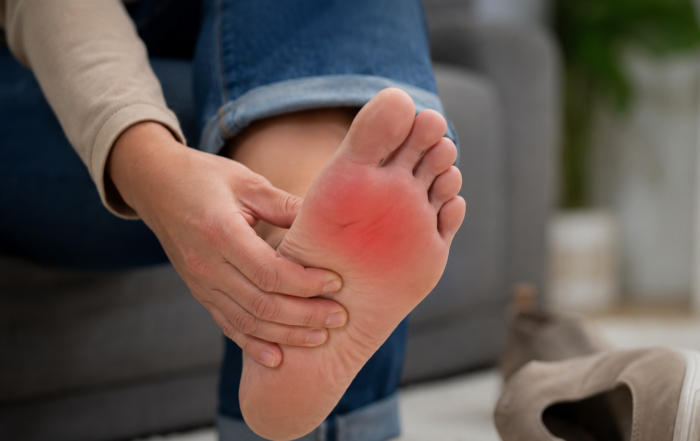 Close-up photograph of a person holding the bottom of their foot, with redness highlighting pain in the ball of the foot and a shoe resting nearby.